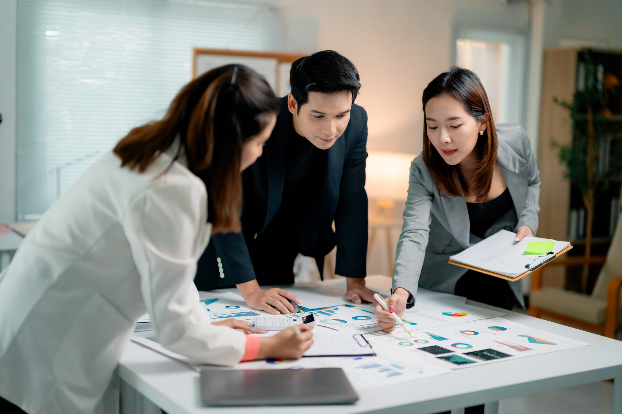 Corporate team collaborating, examining financial charts, strategizing business development An Asian corporate team collaboratively analyzing financial charts and reports, demonstrating strategic insights for KPO solutions.