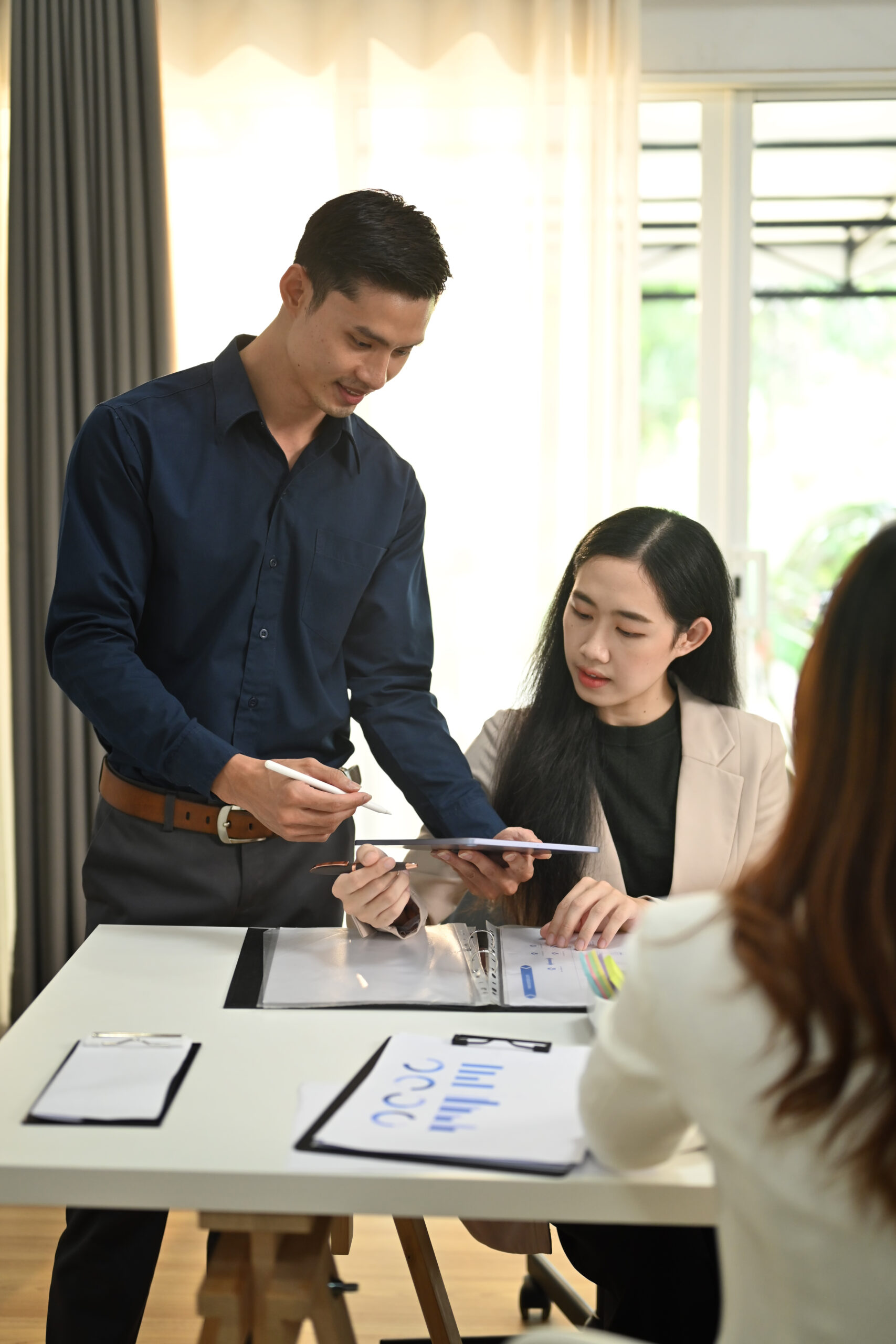 Asian male manager sharing ideas business strategy, discussing f Asian male manager discussing financial data on a tablet with a female colleague, demonstrating collaborative outsource financial services.