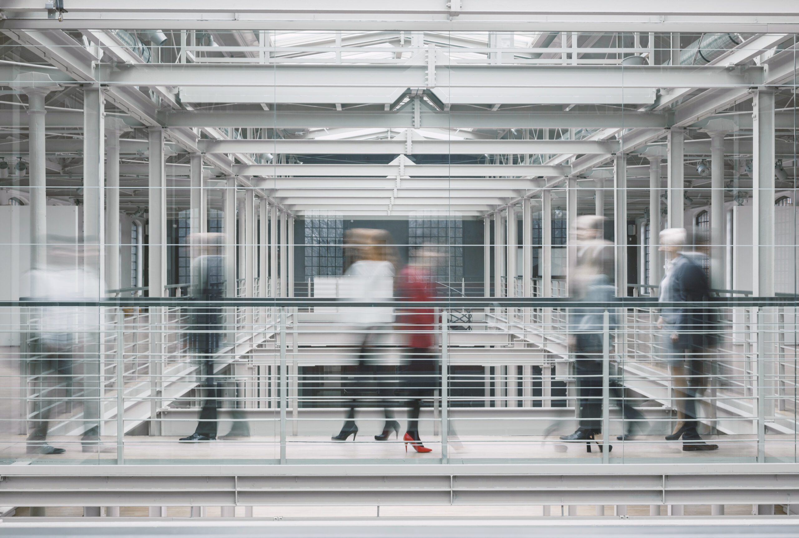 Blurred professionals walking through a modern glass office walkway, symbolizing the dynamic nature of business process services at Beehive.